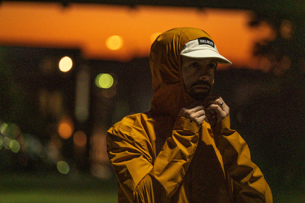 A man zipping up an orange jacket janji rainrunner