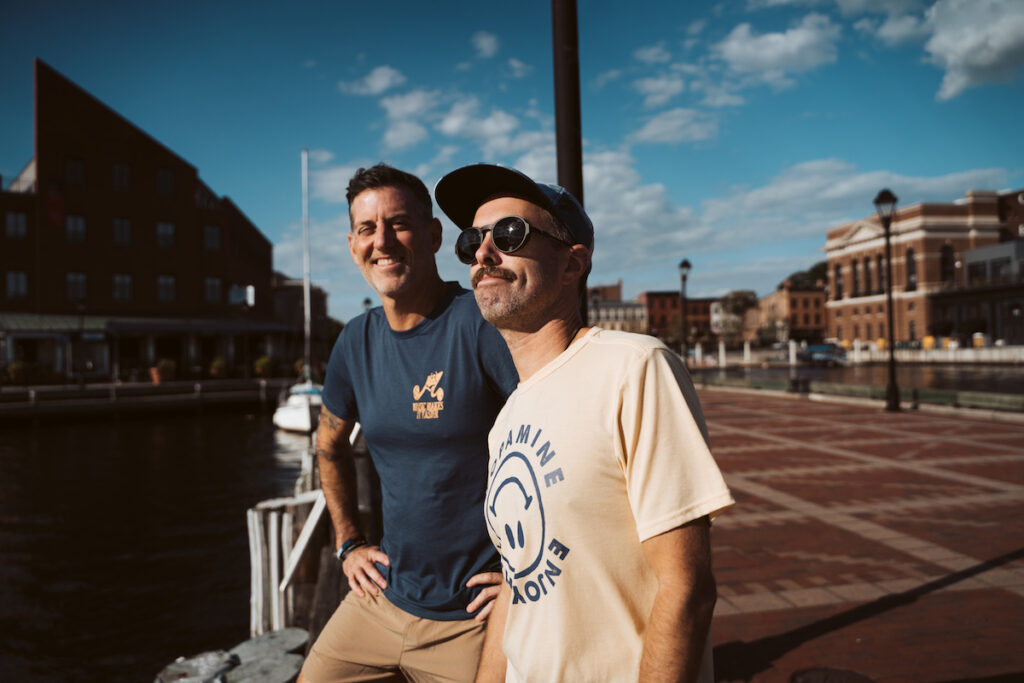 two men outside with a blue sky in the background, smiling