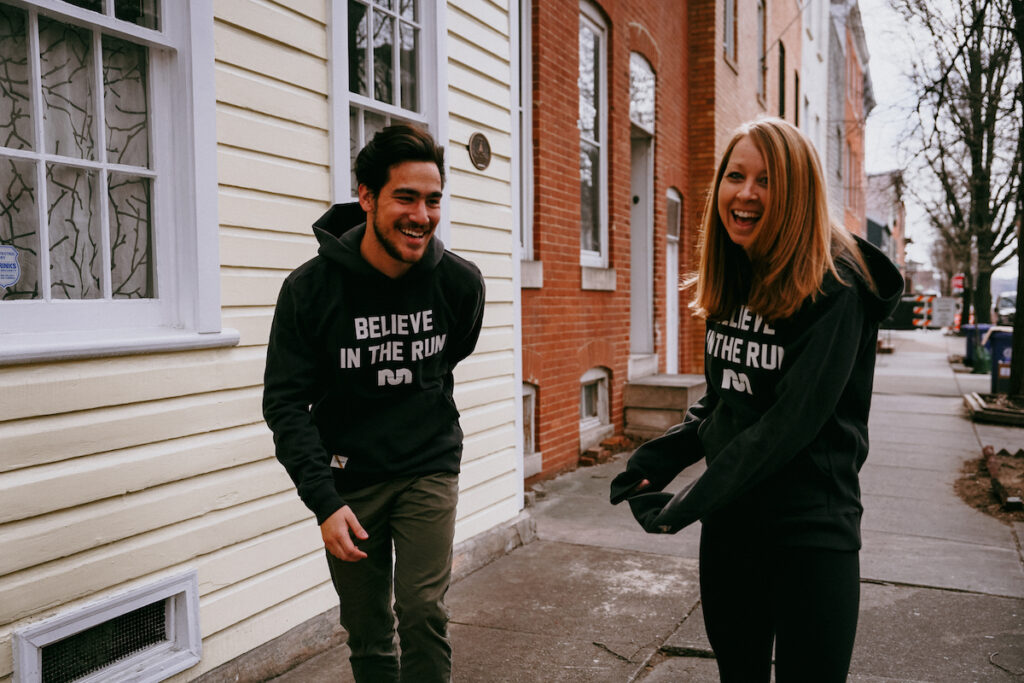 a man and woman laughing in running gear on a sidewalk