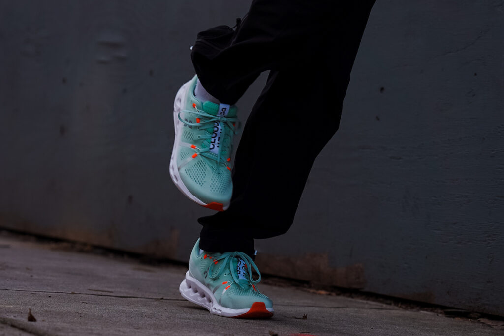 photo of black pants running in a teal pair of on cloudsurfer running shoes