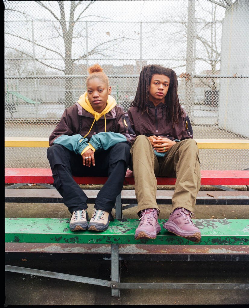 a girl and boy sitting on a multi-colored bleacher wearing hoka x bodega urban hiker collab