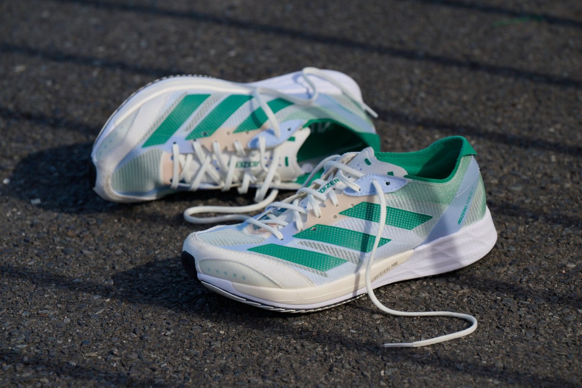 white and green adidas adios 7 running shoe on pavement