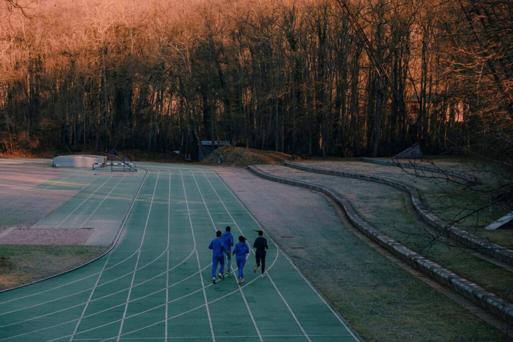 four runners on a green track at sunrise