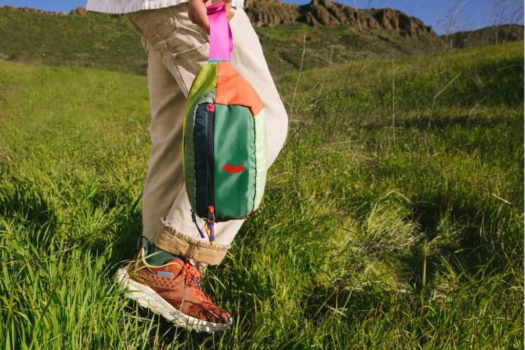 legs of someone wearing khaki pants carrying Cotopaxi Kapai 3L Hip Pack and wearing hoka anacapa trail shoes