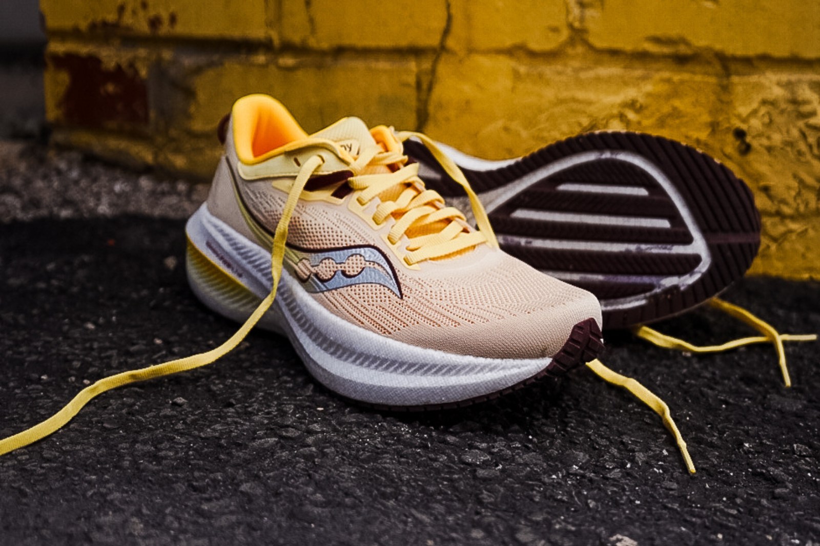 yellow saucony shoe with hellow laces and yellow brick wall in the background