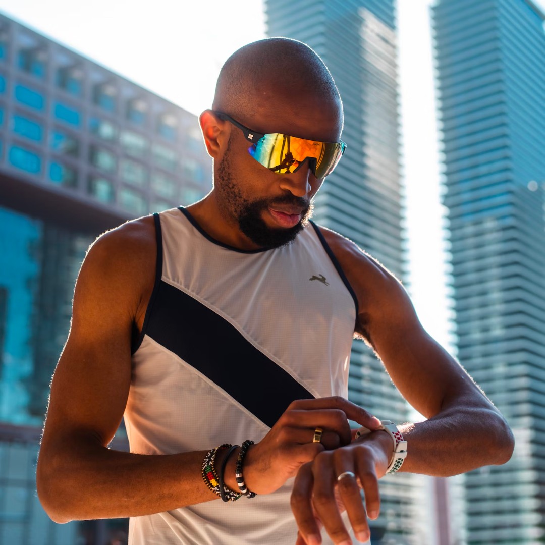 A man wearing sungod sunglasses in front of tall buildings.