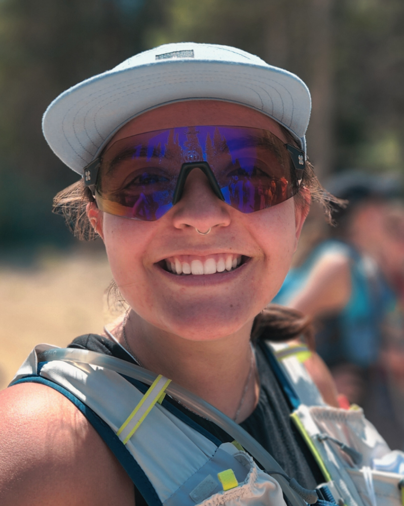A woman wearing sunglasses and a hat is smiling.