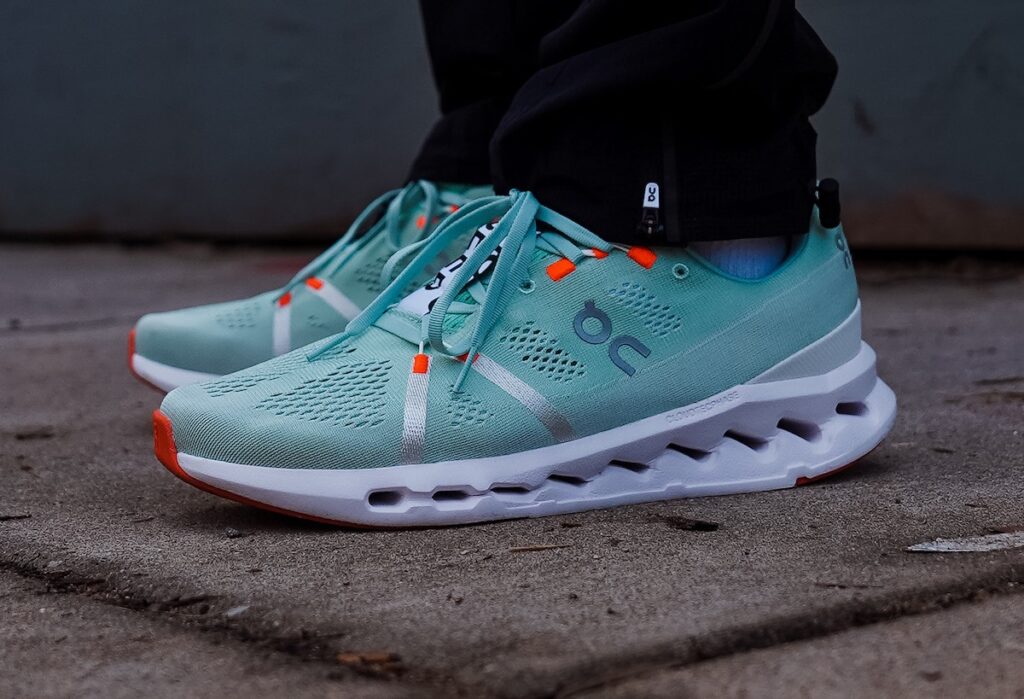 side look at teal on cloudsurfer running shoes with white midsole and orange accents