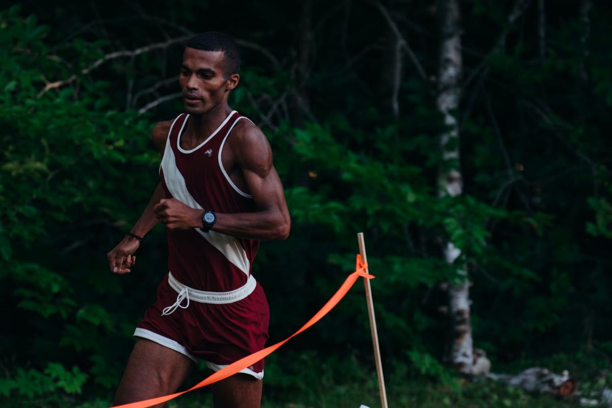 man running in tracksmith gear with woods in the background