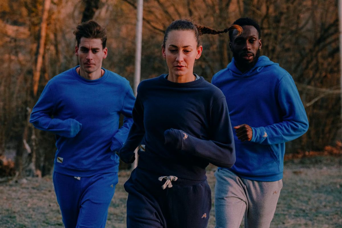 woman running in center in sweatshirt and sweatpants with two men running to the sides behind her