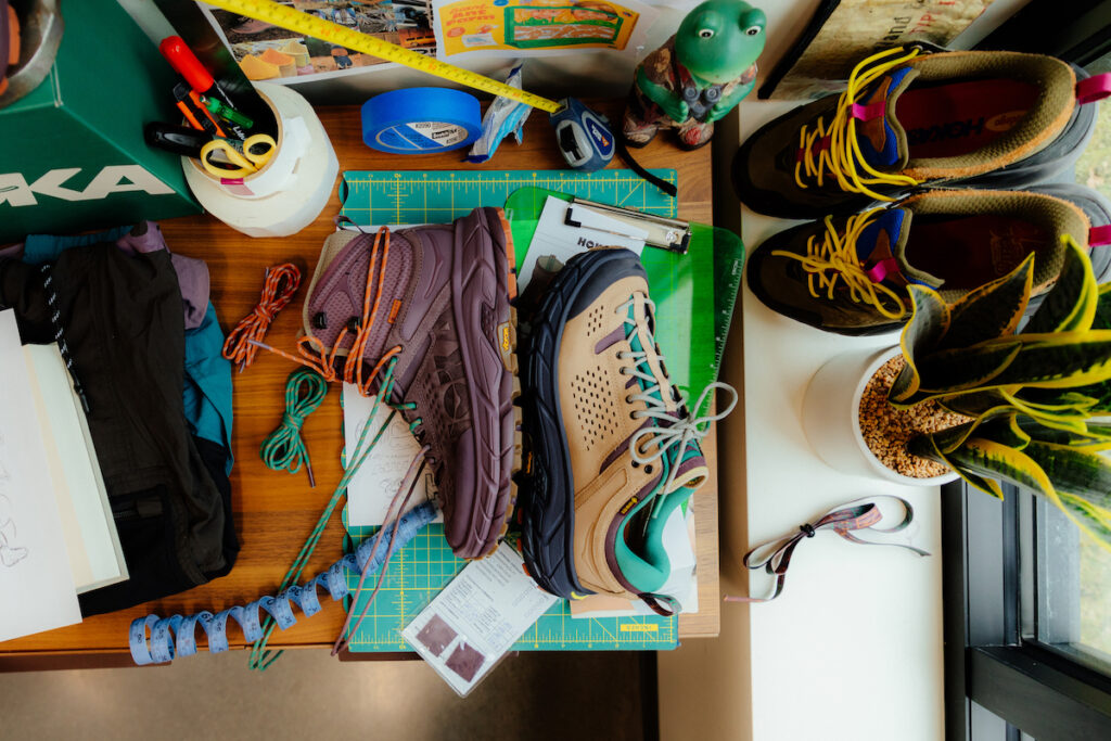 purple hoka hiking boot and brown hoka hiking shoe on a messy workbench