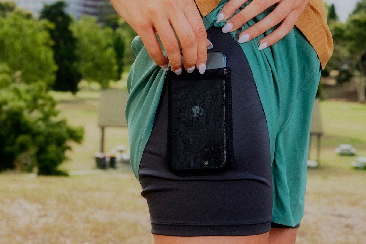 woman putting an iphone into the side pocket of a black running short liner