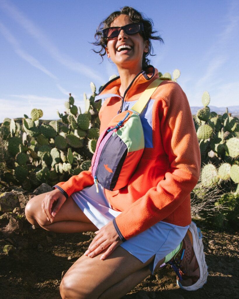 girl smiling in the desert wearing colorful clothing, kneeling on ground