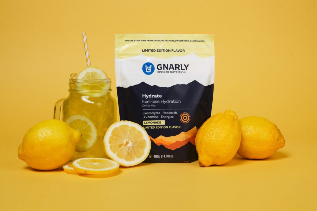 bag of gnarly hydration mix with lemons and a glass of lemonade on a yellow background