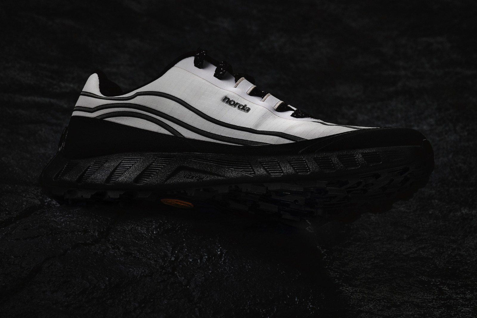 white trail shoe with black midsole on black background