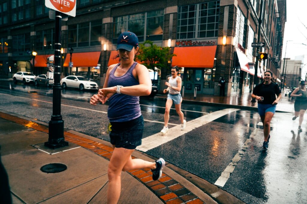 woman in purple tank top and hat running through rainy city streets looking at a watch