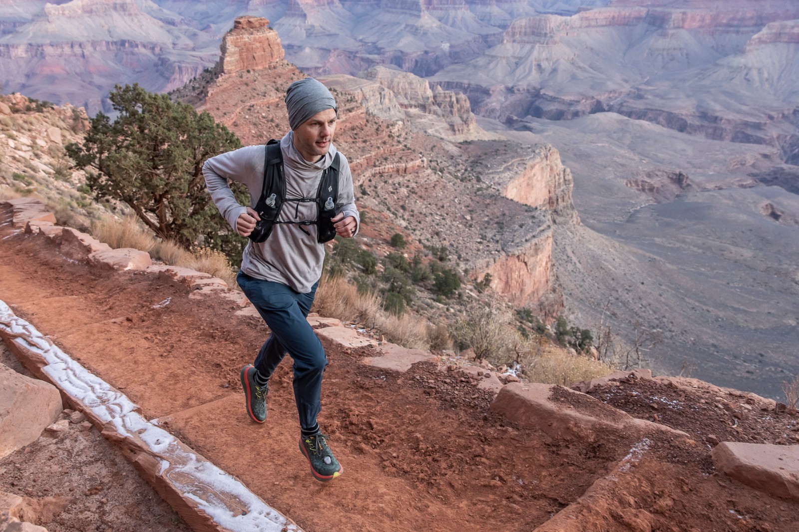 man running on dirt path above the grand canyon
