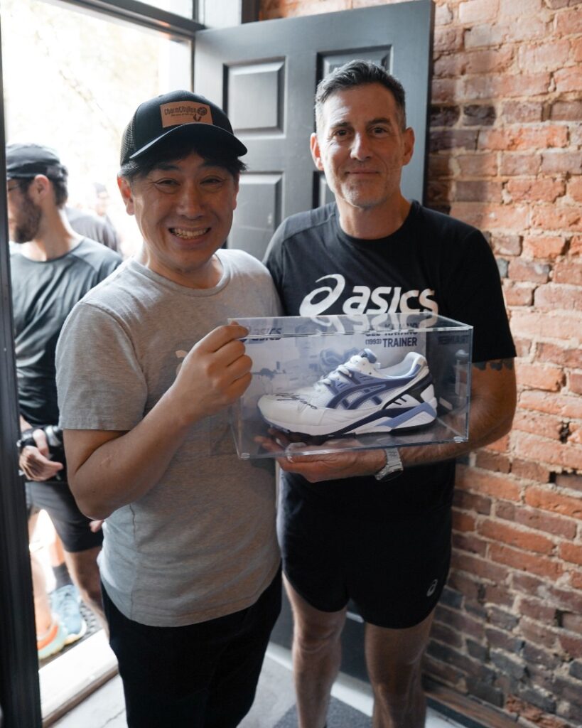 Two men holding a box of asics shoes during a party recap.