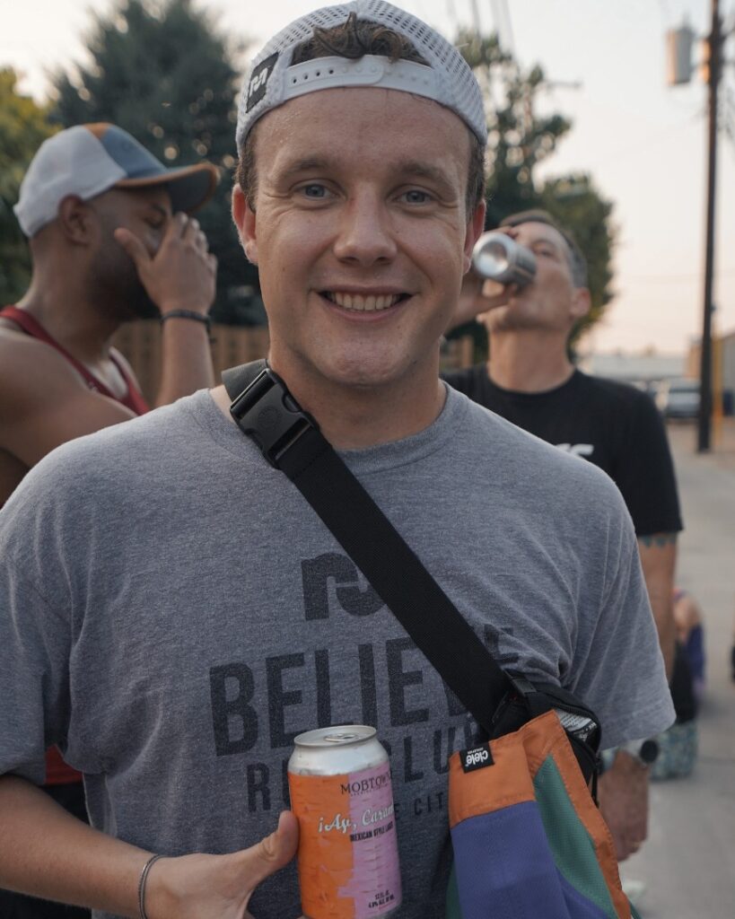 man smiling and holding two cans of beer